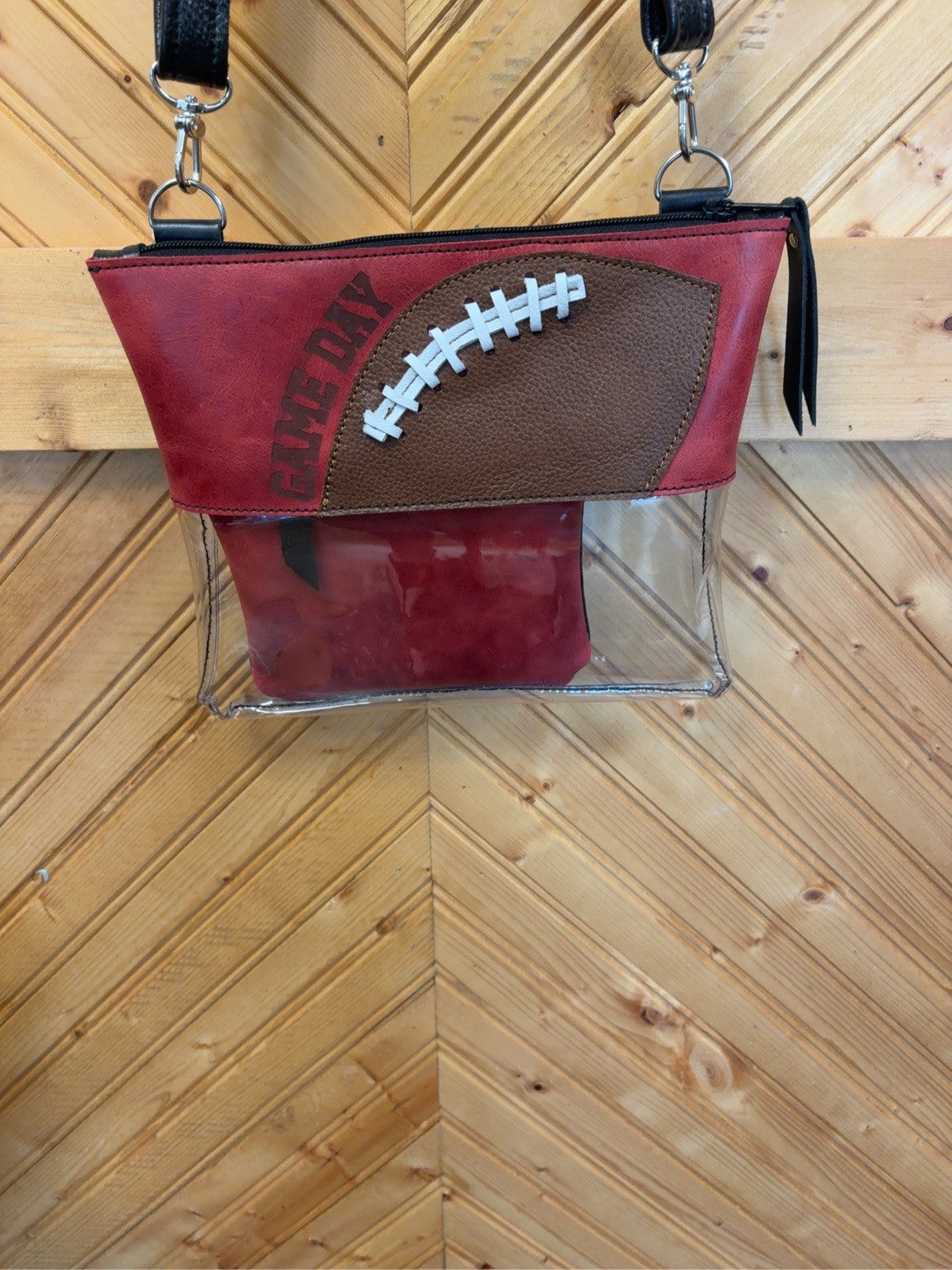 Burgundy Arena crossbody bag with a brown football detail, white laces, GAME DAY lettering, clear lower body, black strap and included burgundy pouch