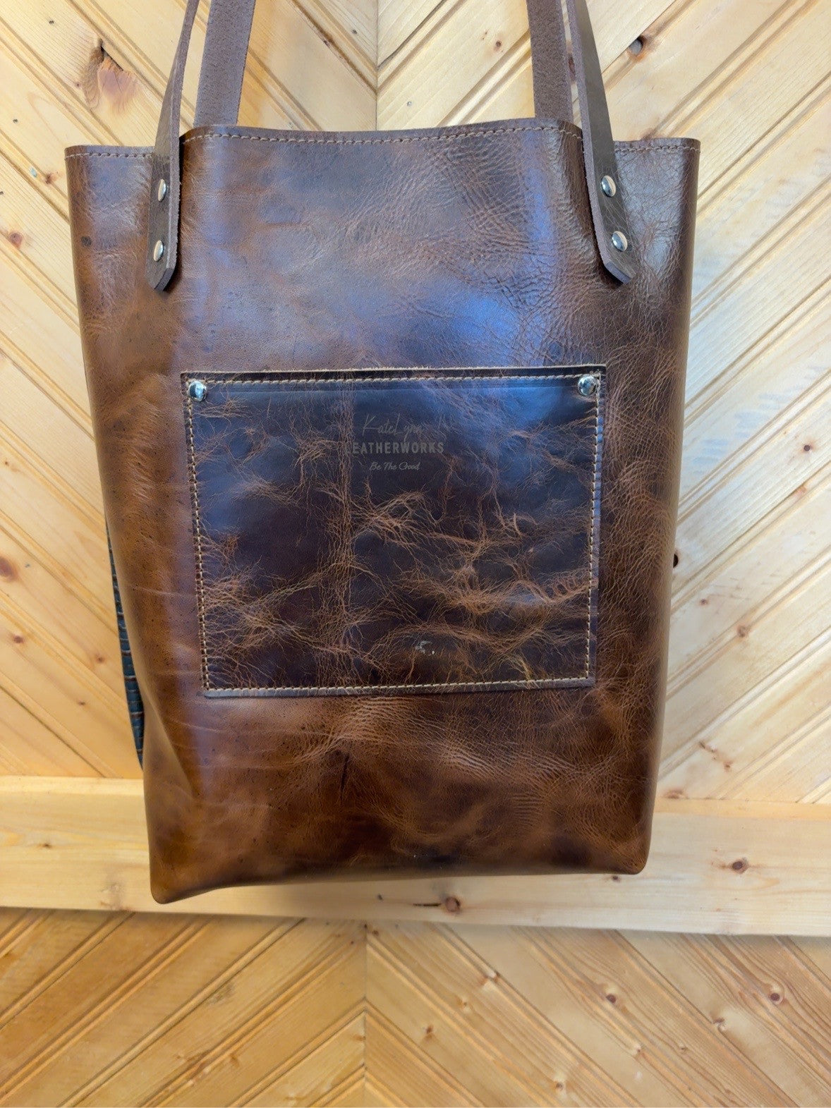 Brown back of Bristow Bookbag with an exterior patch pocket, KateLynn Leatherworks logo and two shoulder straps