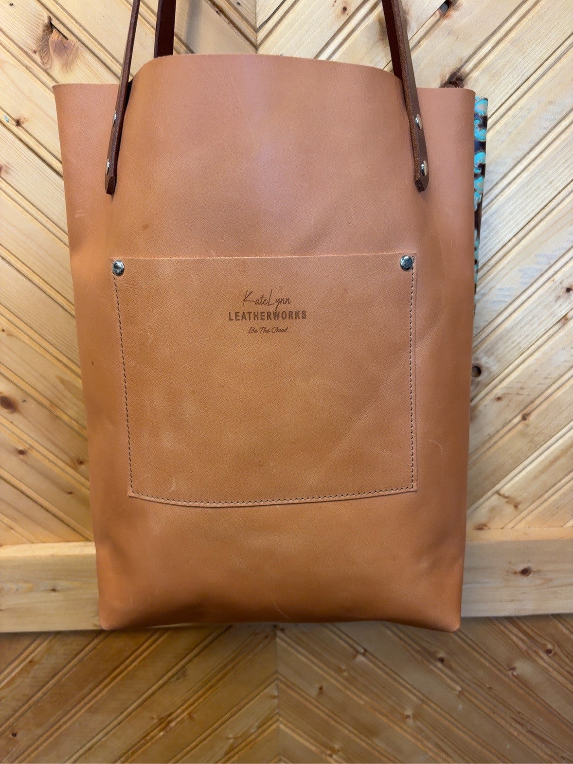 Tan back of the Bristow Bookbag showing a matching exterior pocket with the KateLynn Leatherworks logo, brown shoulder straps and silver-tone rivets.