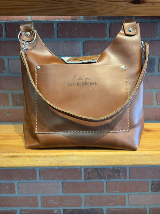 Back of brown Lex shoulder bag showing the exterior slip pocket, KateLynn Leatherworks logo and brown shoulder strap.