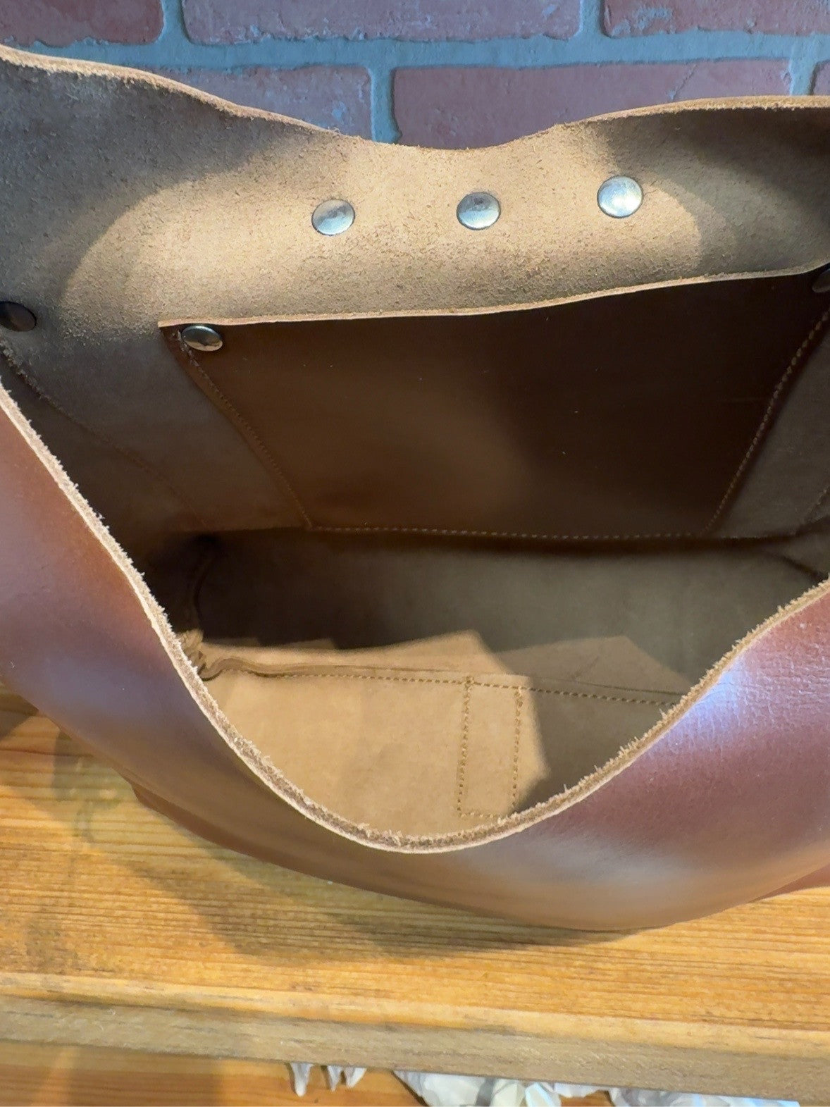 Interior of brown Lex shoulder bag showing its inside pocket and stitched seams.