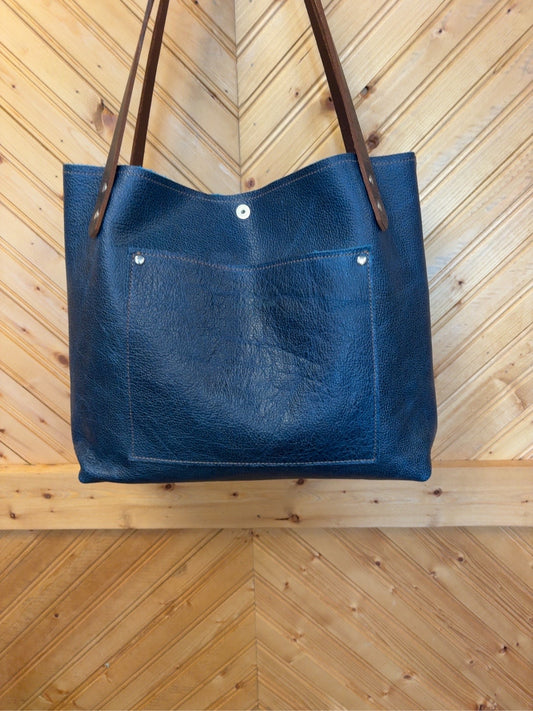 Back of the blue Tucson tote showing the matching exterior slip pocket, snap closure and brown shoulder straps.