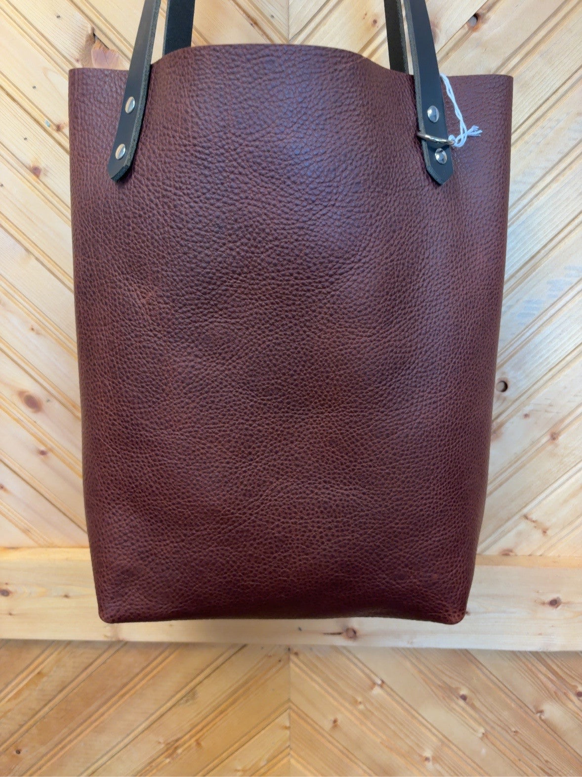 Mahogany pebble-grain leather Bristow bookbag with black shoulder straps, shown from the plain side.