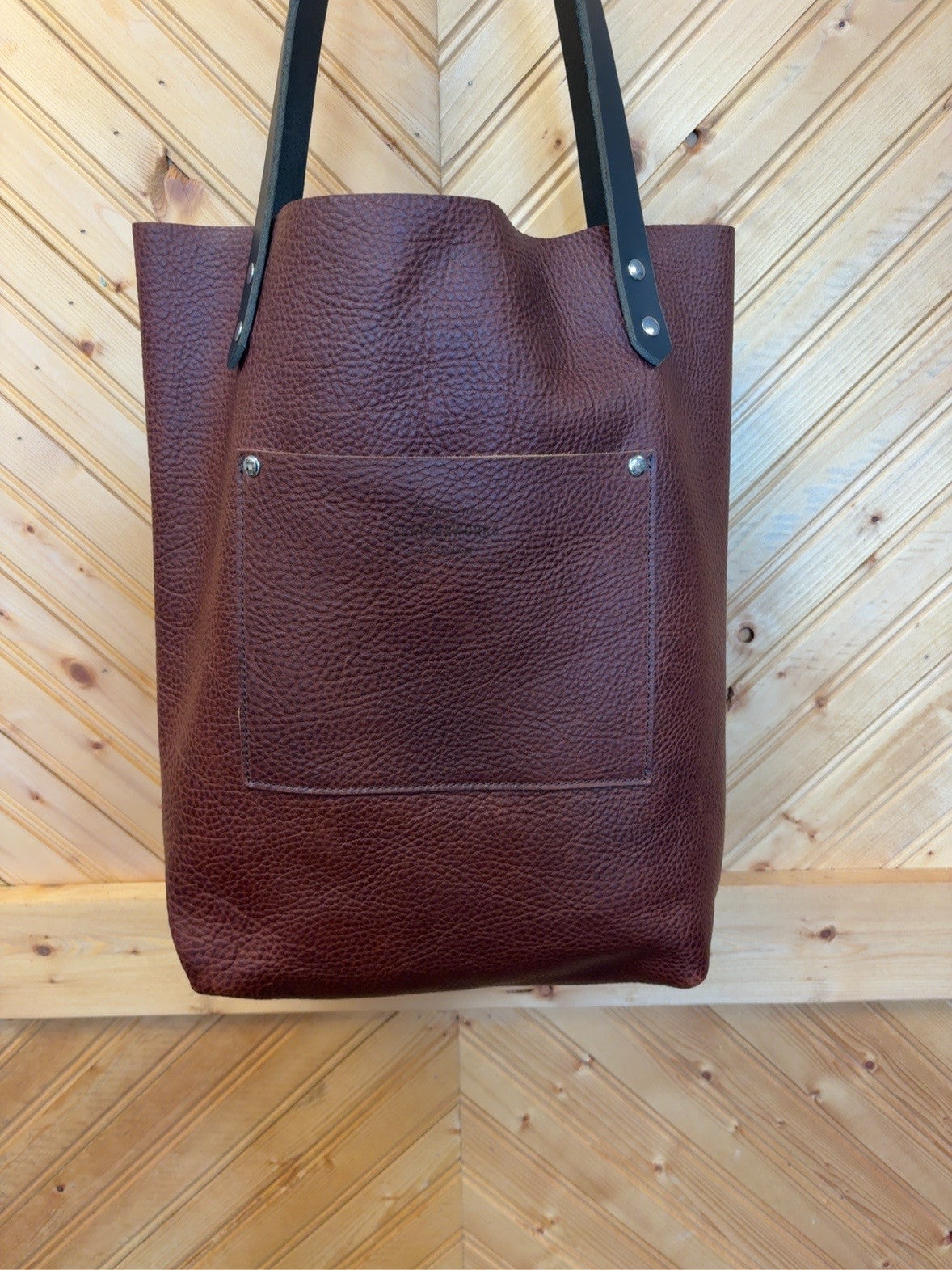 Mahogany pebble-grain leather Bristow bookbag showing a matching exterior pocket and black shoulder straps.