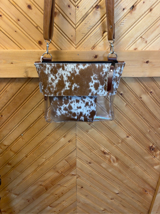 Brown-and-white cowhide Arena crossbody bag with a clear lower body, matching pouch, brown leather strap and zip-top closure.