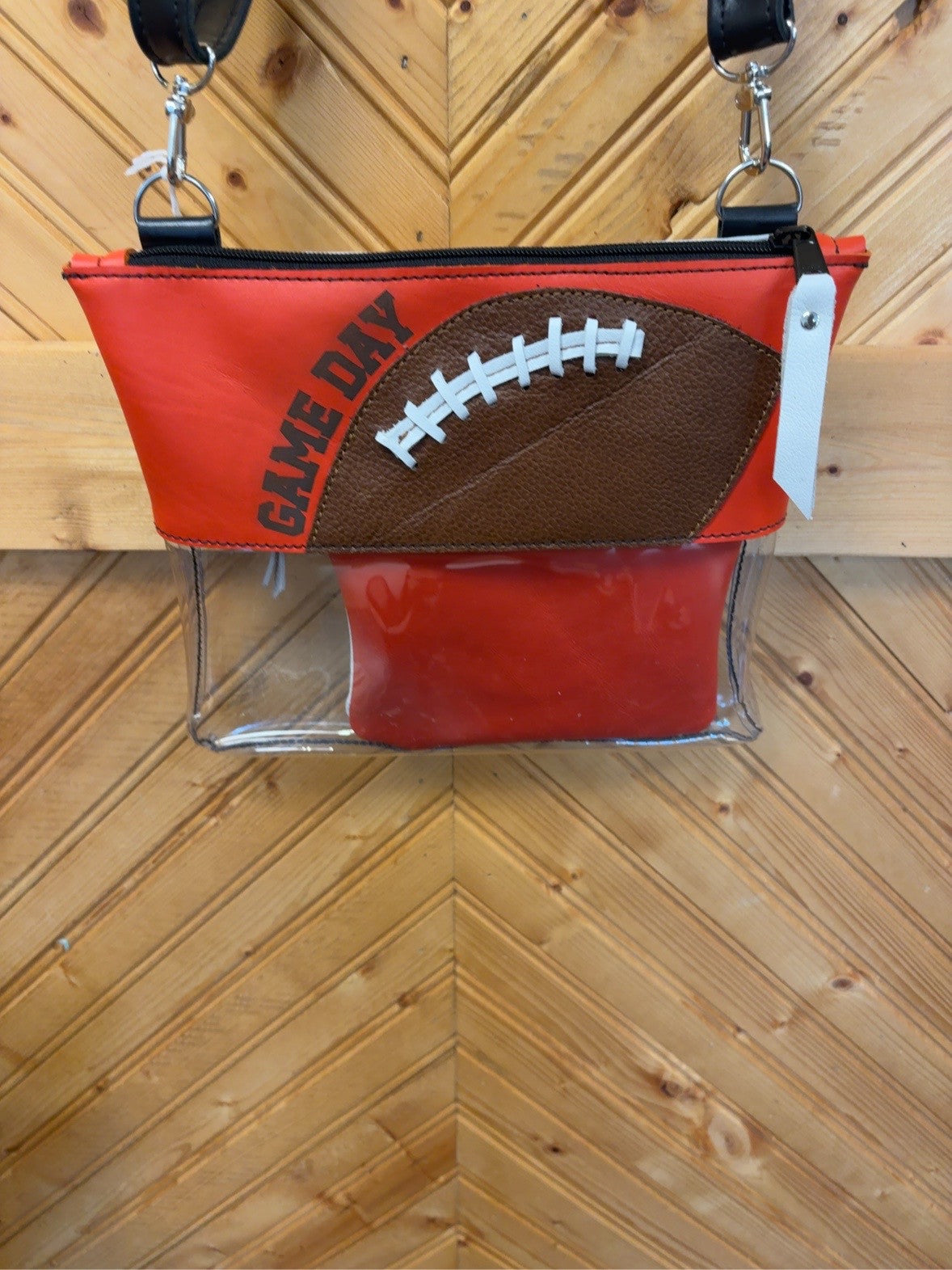 Orange Game Day Arena crossbody bag with a brown football and white lacing, clear lower body, black strap and matching orange pouch.