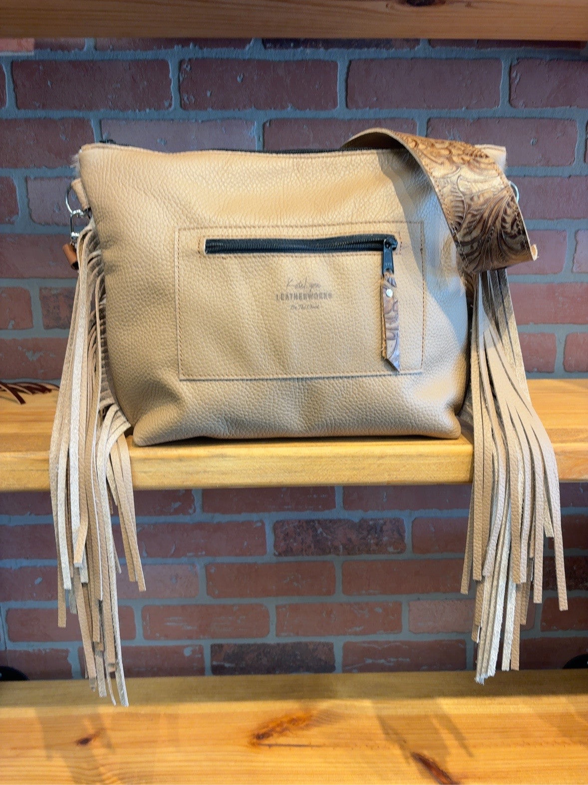 Tan pebble-textured back of the Honey Floral KC bag with an exterior zipper pocket and long side fringe.