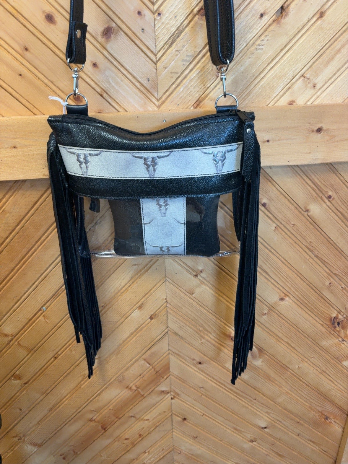 Black Arena crossbody bag with silver-toned skull detailing, clear lower body, long black side fringe, zip-top closure and matching pouch