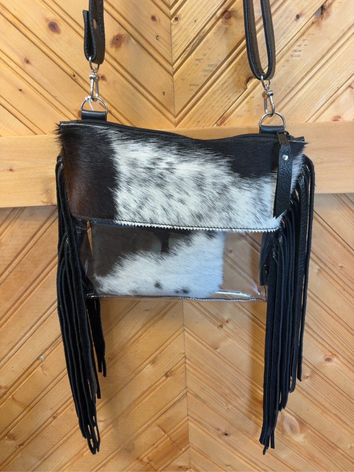 Black-and-white cowhide Arena crossbody bag with clear lower body, long black fringe, zip top and matching pouch