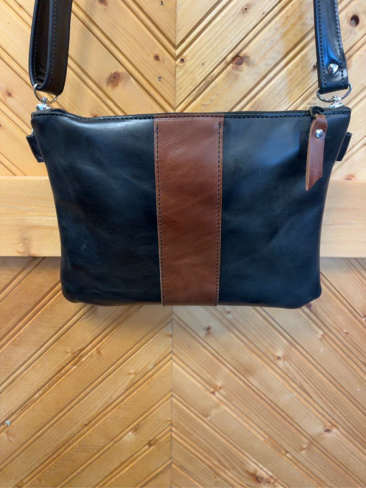 Austin bag with a black exterior, broad brown center stripe, brown zipper pull and black strap