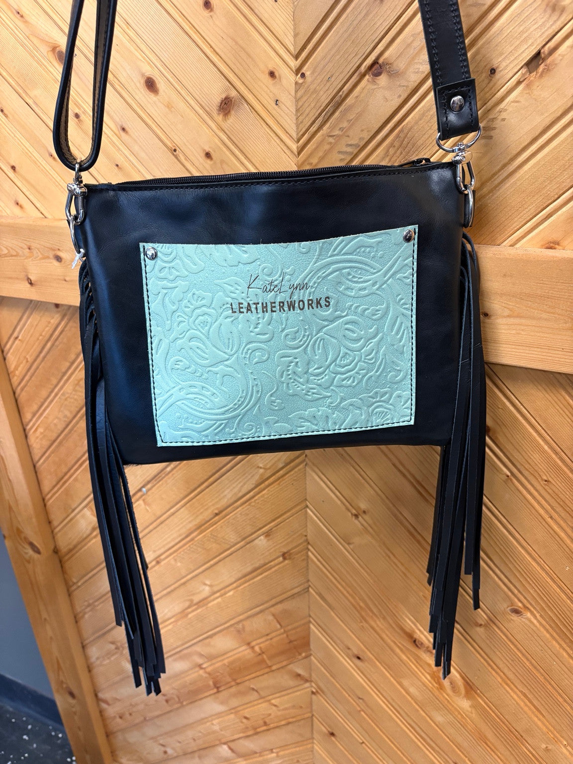Black back of the Austin bag with mint floral embossed pocket, black strap and side fringe