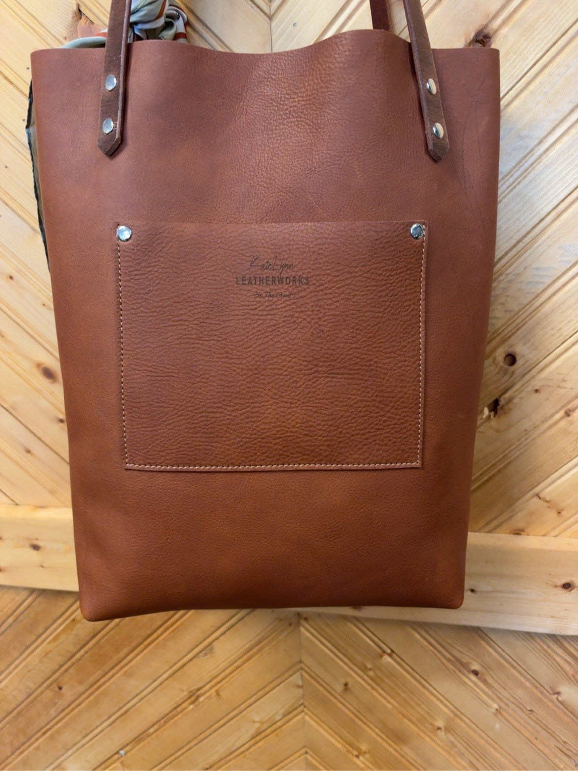 Back of the Brown Floral Bristow Bookbag showing the brown exterior pocket, KateLynn Leatherworks stamp and riveted shoulder straps.