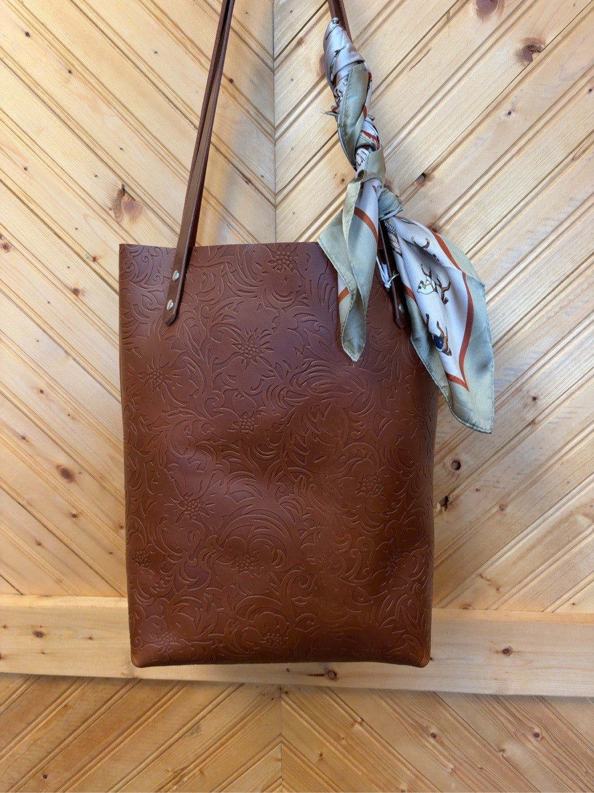 Front of the Brown Floral Bristow Bookbag with brown embossed floral pattern and brown shoulder straps. Scarf shown is not included.