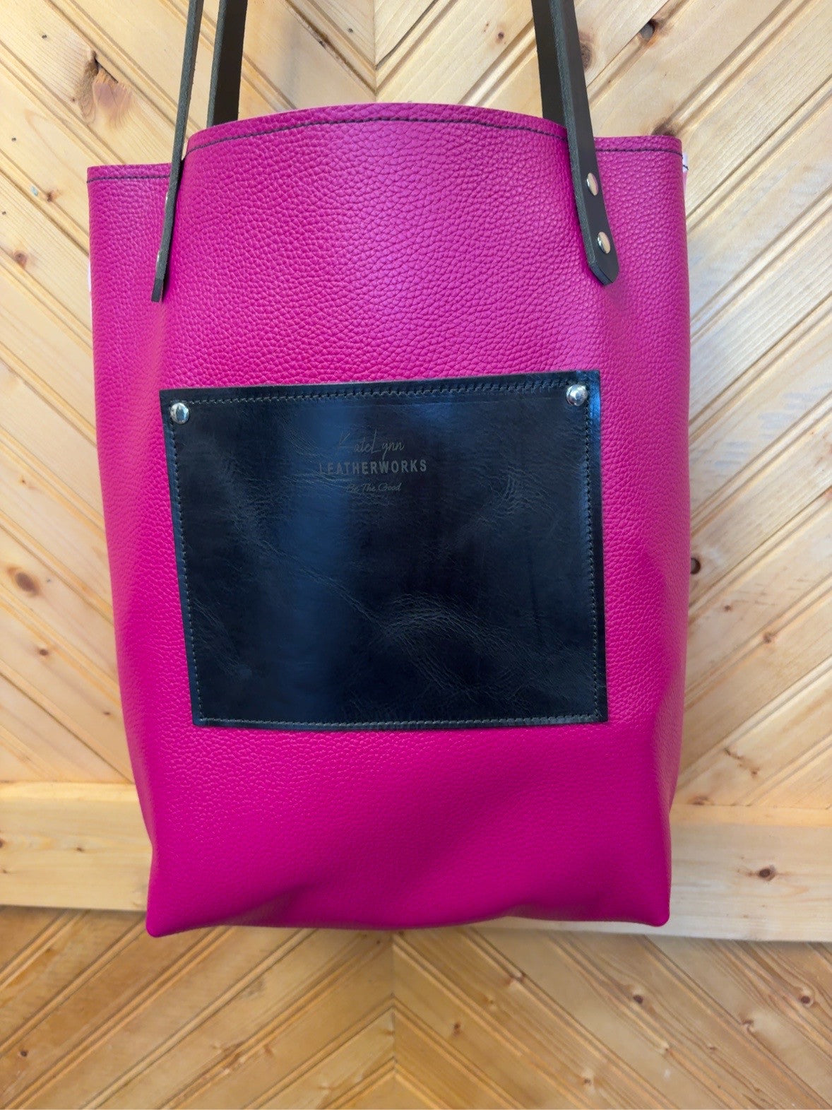 Bright pink back of the Bristow Bookbag showing a black exterior pocket, KateLynn Leatherworks stamp, black shoulder straps and silver-tone rivets.