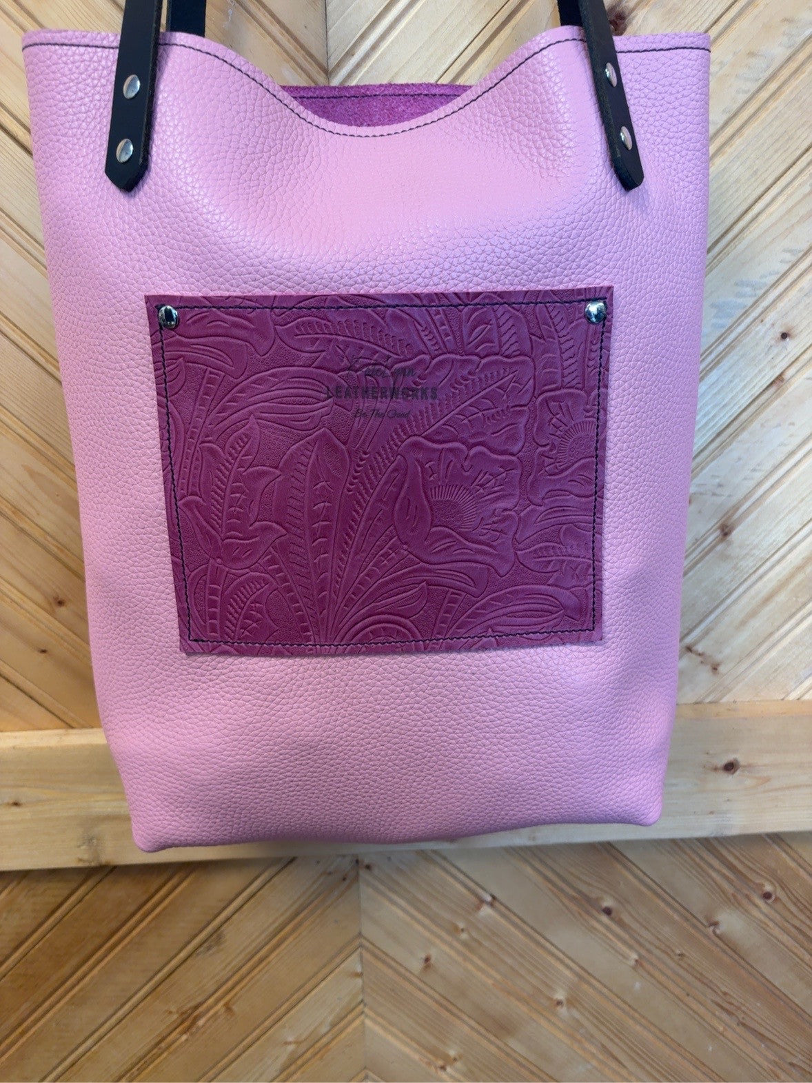 Pink back of the Bristow Bookbag with a rouge embossed floral exterior pocket, KateLynn Leatherworks stamp and black shoulder straps.
