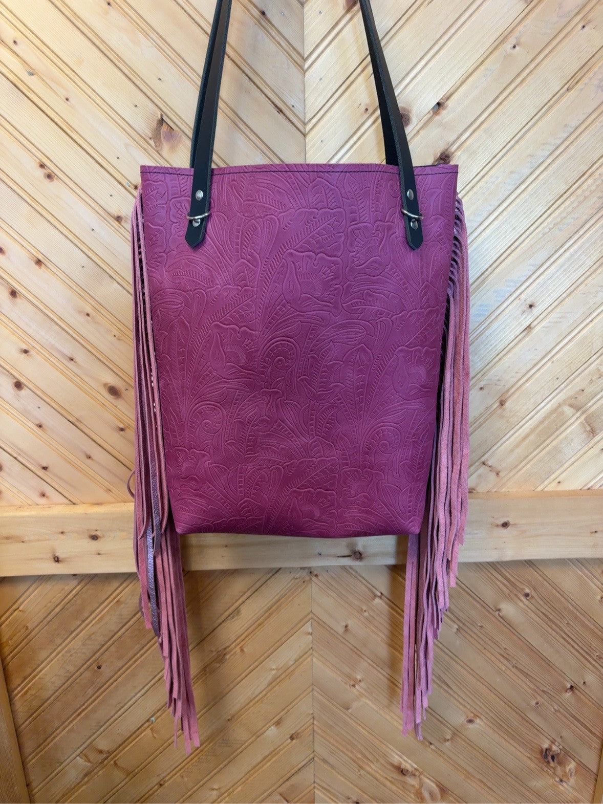 Front of Bristow bookbag with magenta scrolling floral pattern, long pink side fringe and black shoulder straps.