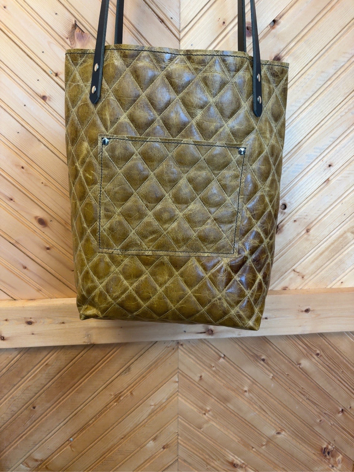 Back of olive-brown diamond-pattern Bristow bookbag showing the exterior pocket and black shoulder straps.