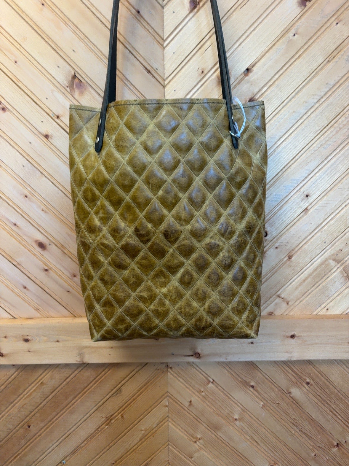Front of olive-brown diamond-pattern Bristow bookbag with black shoulder straps and silver-tone rivets.