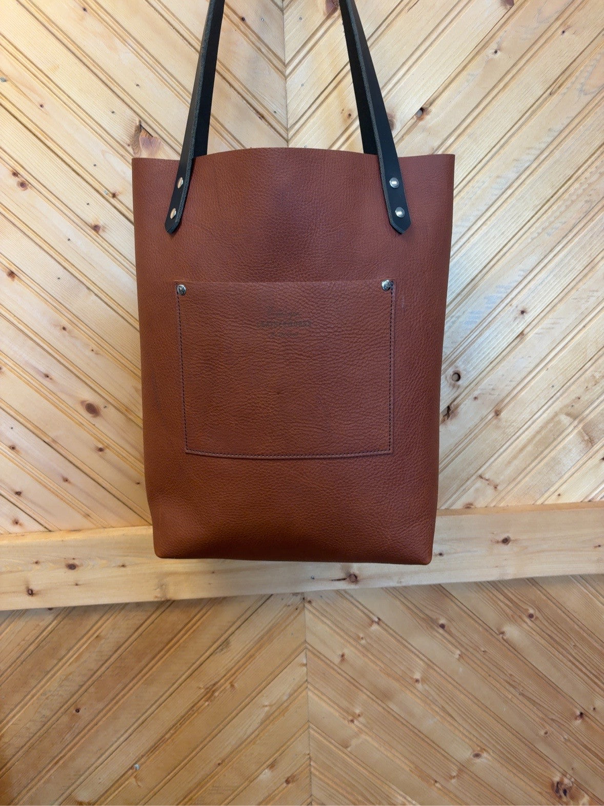 Back of rich brown pebble-grain Bristow bookbag showing the exterior patch pocket and dark shoulder straps.