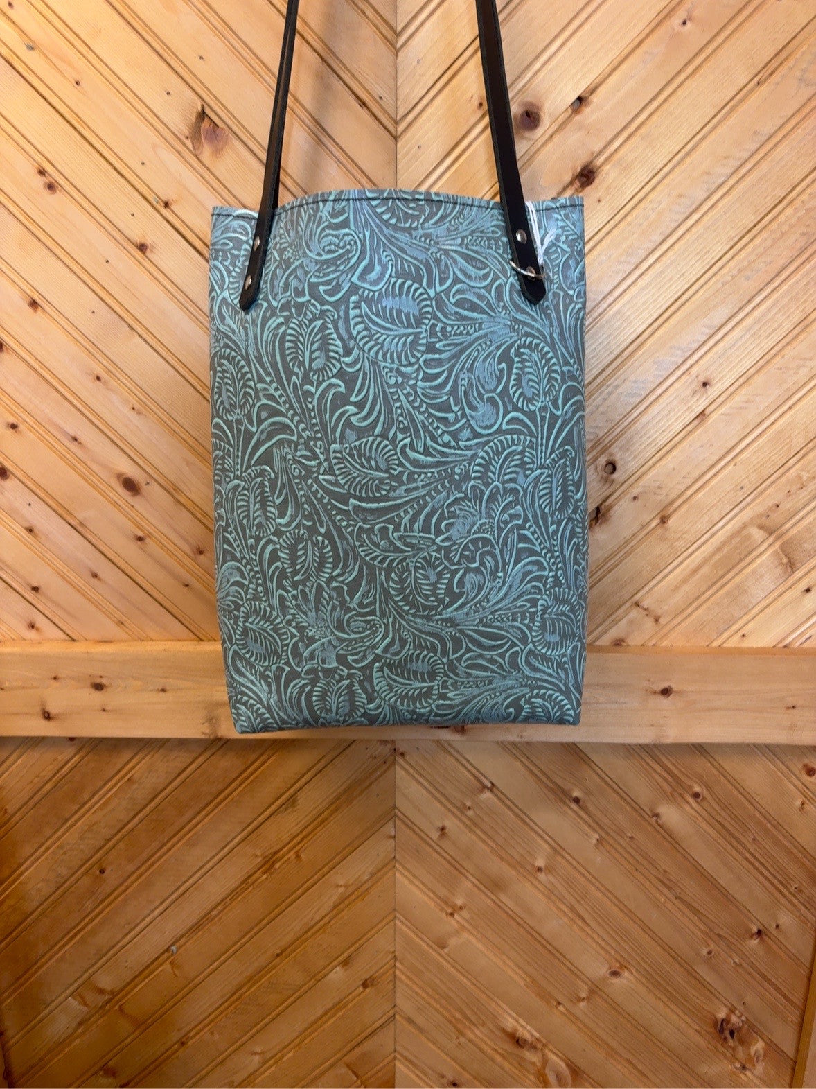 Front of Bristow bookbag with turquoise scrolling floral pattern on a dark background and black shoulder straps.
