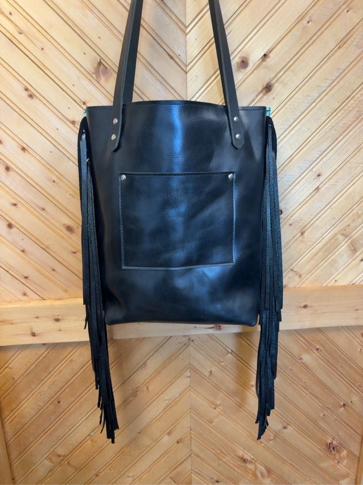 Black back of Bristow bookbag with an exterior patch pocket, long black fringe, black shoulder straps and silver-tone rivets.