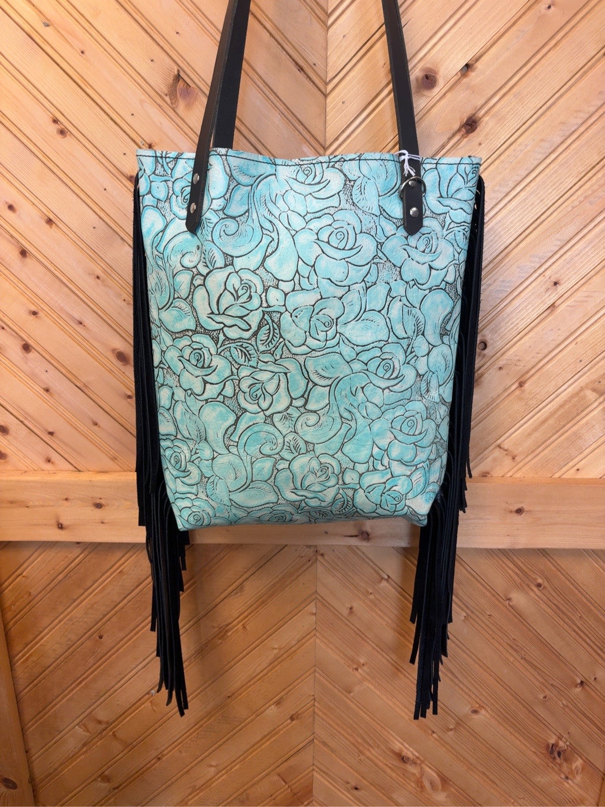 Front of Bristow bookbag with turquoise rose pattern, long black side fringe and black shoulder straps.