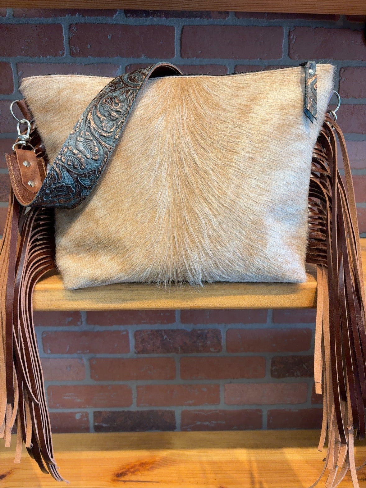 Front of golden-tan cowhide KC bag with brown fringe and blue-and-copper-tone patterned shoulder strap.