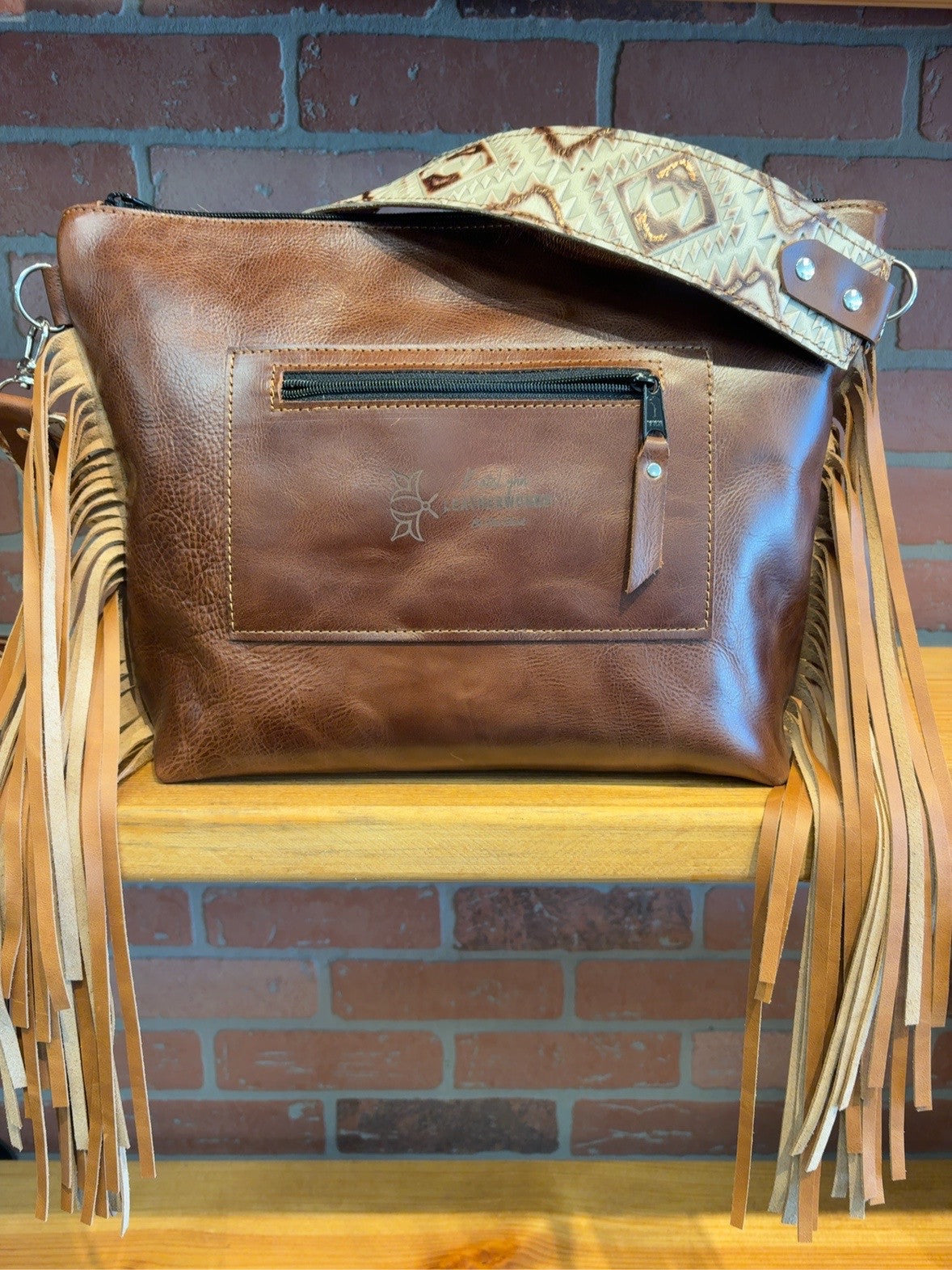 Brown back of KC bag with rear zipper pocket, patterned shoulder strap and long tan side fringe.