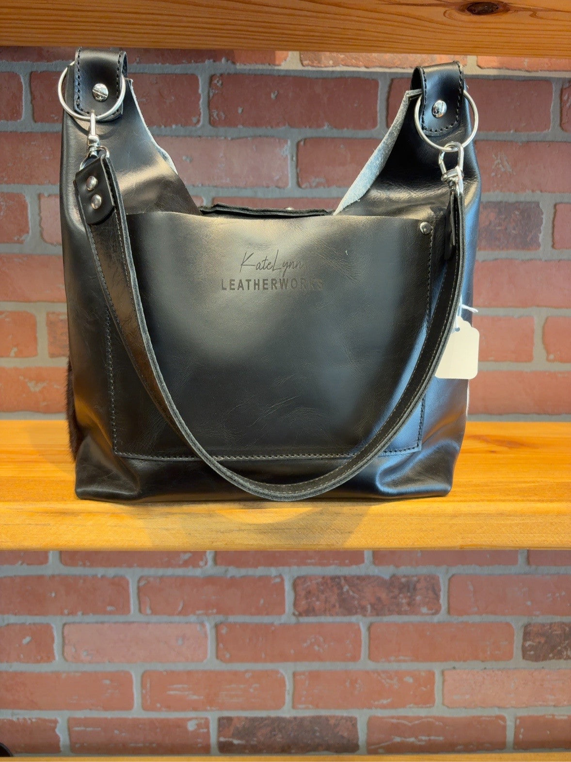 Black leather back of Lex shoulder bag showing the slip pocket, KateLynn Leatherworks logo and matching shoulder strap.
