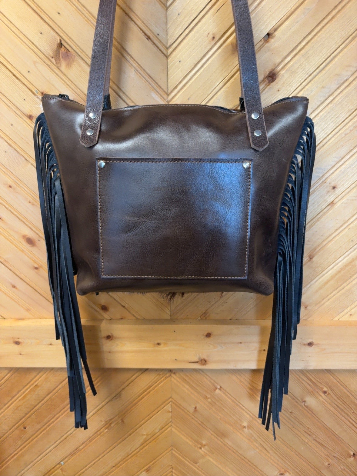 Dark brown back of Tucson Mini showing the exterior slip pocket, shoulder straps, zipper top and black side fringe