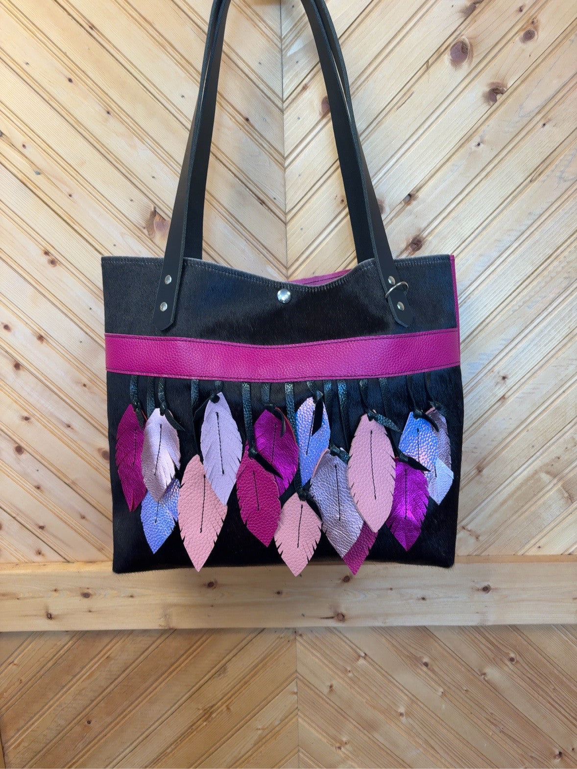 Front of the Tucson tote with black cowhide, magenta trim and layered handcut leather feathers in pink, purple and shimmering tones.