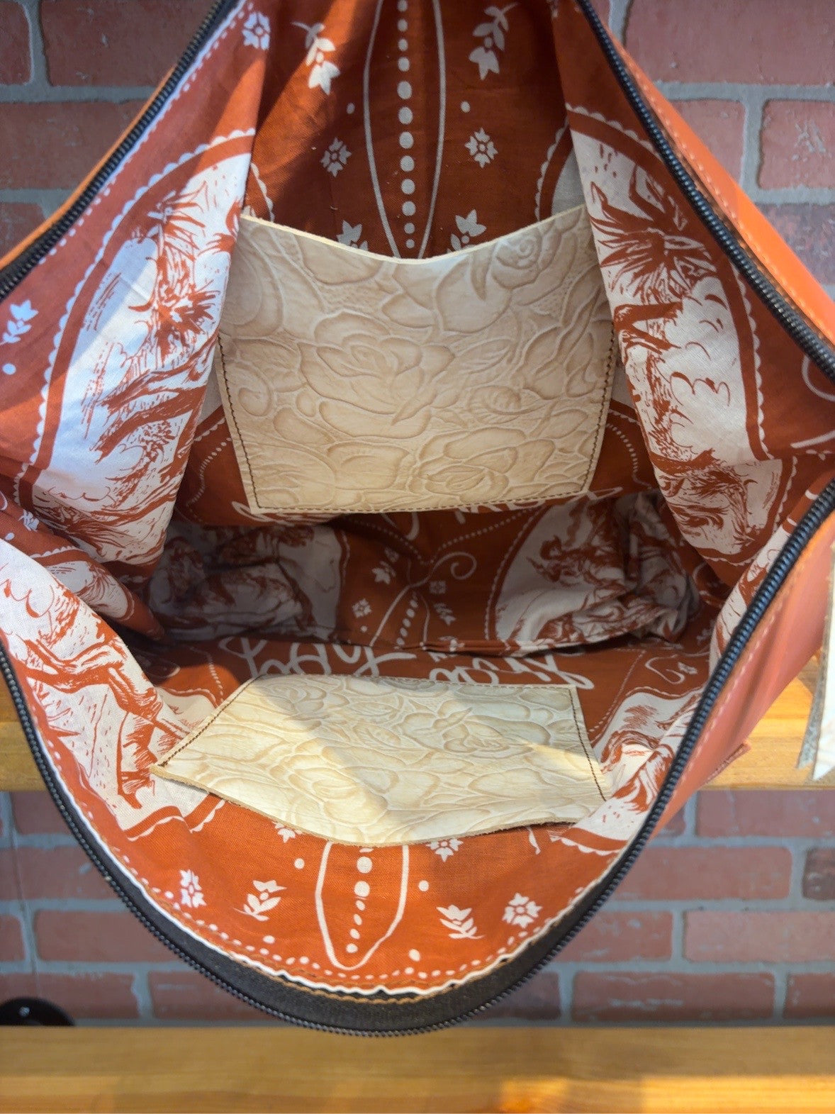 Interior of the Tucson tote showing orange-and-ivory patterned lining and two ivory rose-pattern slip pockets.